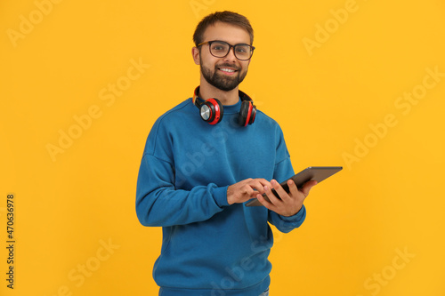 Student with headphones using tablet on yellow background