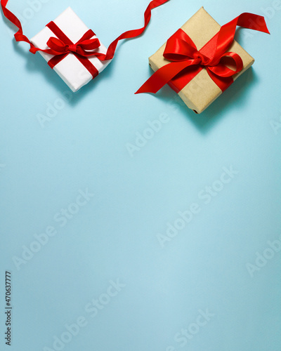 Two white brown paper gift boxes with a red satin ribbon bow and happy birthday sign on top on blue background. Christmas holiday mother and father Valentines days flat lay concept with copy space.