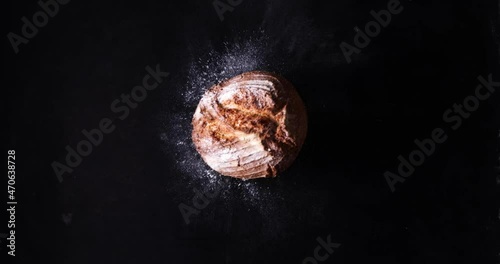 Fresh loaf of bread scattering flour against black background photo