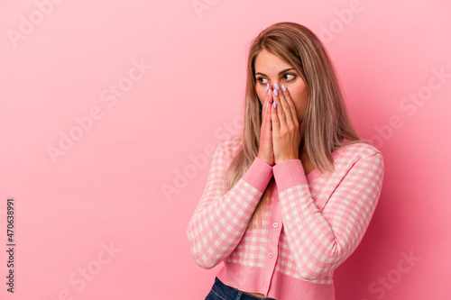 Young russian woman isolated on pink background thoughtful looking to a copy space covering mouth with hand.