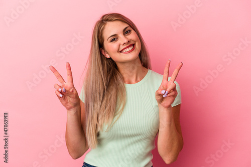 Young russian woman isolated on pink background showing victory sign and smiling broadly.