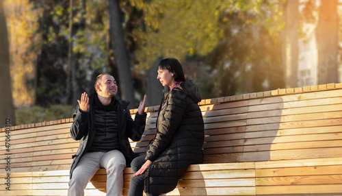 Man emotionally gesturing with his hands tells something to woman, sitting on bench in the park. Selective focus