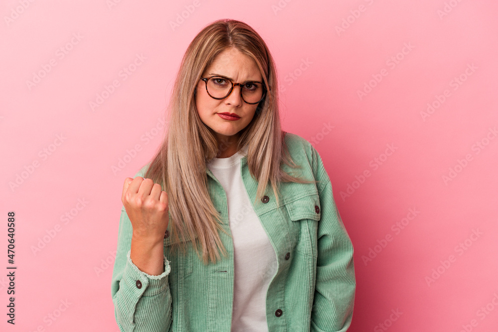Young russian woman isolated on pink background showing fist to camera, aggressive facial expression.