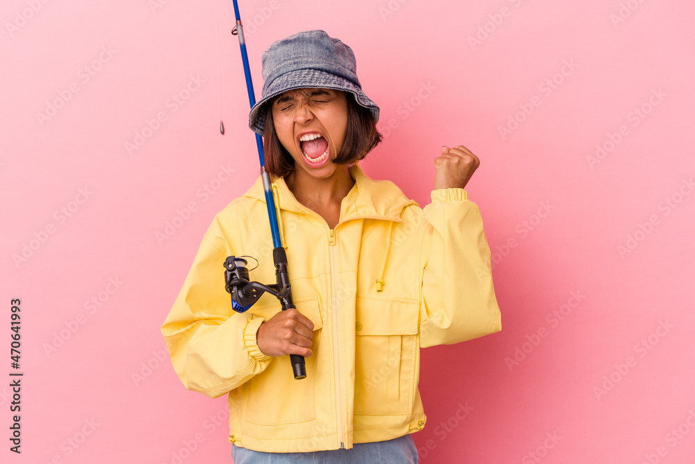 Young mixed race woman practicing fishing isolated on pink background raising fist after a victory, winner concept. Young mixed race woman practicing fishing isolated on pink background raising fist after a victory, winner concept.