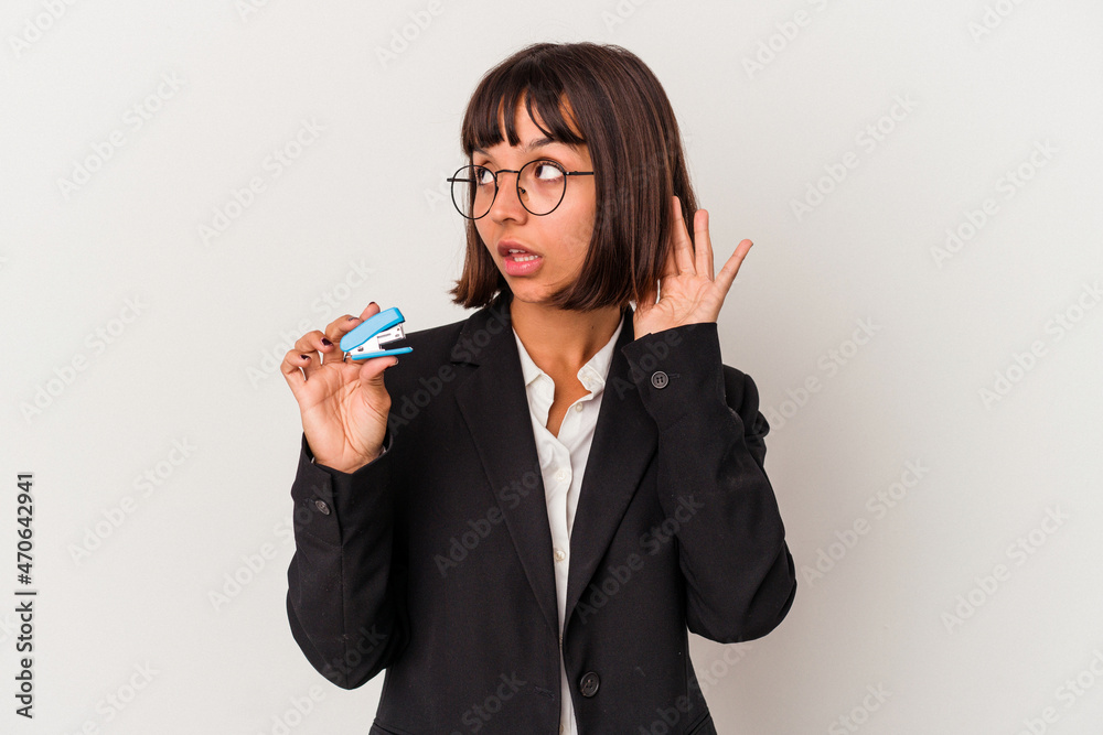 Young mixed race business woman holding a stapler isolated on white background trying to listening a gossip. Young mixed race business woman holding a stapler isolated on white background trying to listening a gossip.