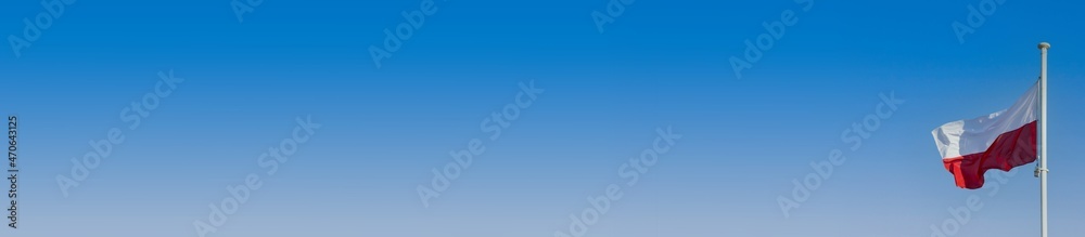 Polish flag flying in the wind on a high mast against the background of blue sky. Panorama.