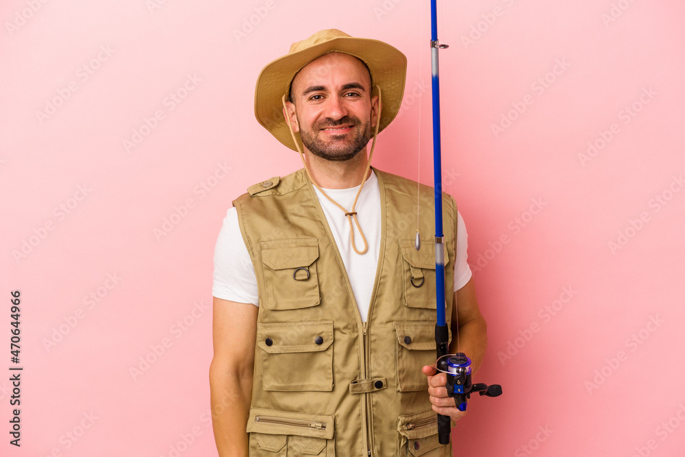 Young bald fisherman holding a rod isolated on pink background happy, smiling and cheerful. Young bald fisherman holding a rod isolated on pink background happy, smiling and cheerful.