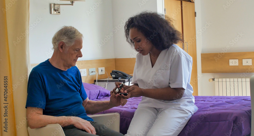 Obraz premium African female doctor visiting elderly male patient in hospital bed. Rehabilitation and retirement concept