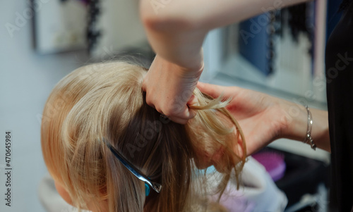 Barber woman make fashionable pretty hairstyle for cute little blond girl