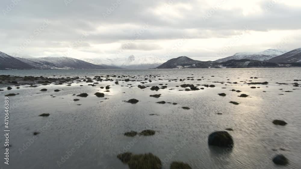 Drone shot flying low over a fjord in Norway with snow-capped mountains Drone shot flying low over a fjord in Norway with snow-capped mountains