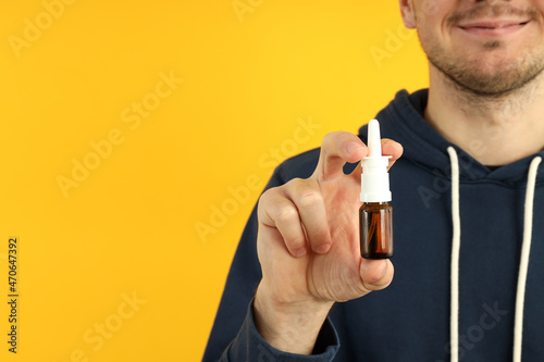 Young man with nasal spray on yellow background, runny nose concept