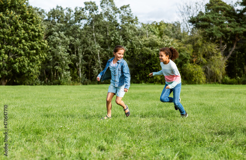childhood, leisure and people concept - happy girls playing tag game and running at park