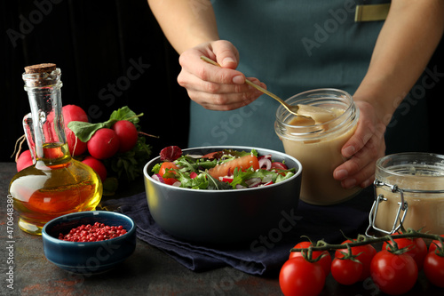 Concept of cooking vegetable salad with tahini sauce on dark textured table