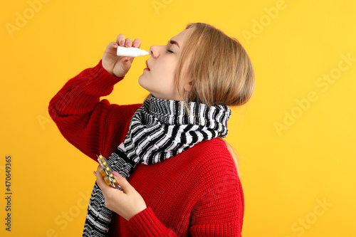 Young woman with nasal drops on yellow background, runny nose concept photo