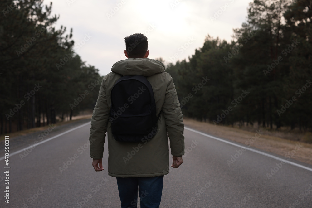 Man with backpack on road near forest, back view Man with backpack on road near forest, back view