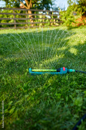 Oscillating garden sprinkler spraying water over green grass at home