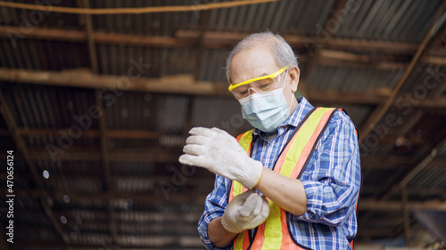 Asian senior male carpenter wearing protective glove for working at carpentry workshop. Man preparing for making a funiture