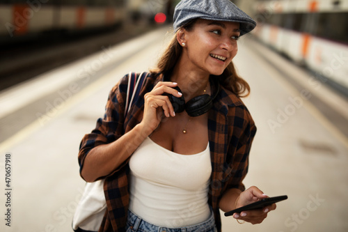 Young woman waiting for the train standing at the railway station. Beautiful girl using the phone while waiting for the train...