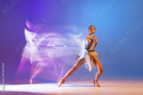 Portrait of young graceful flexible woman dancing ballroom dance without partner isolated on gradient blue purple background in neon mixed light © master1305