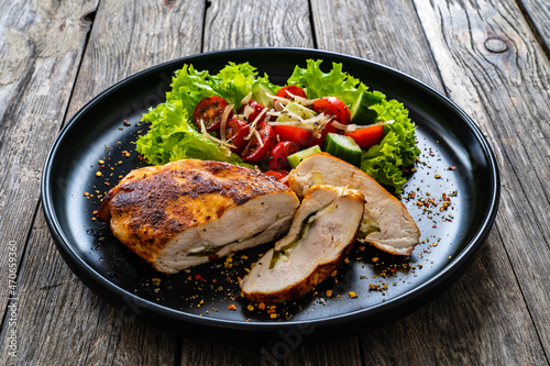 Stuffed chicken breast with mozzarella and fresh vegetable salad on wooden background 