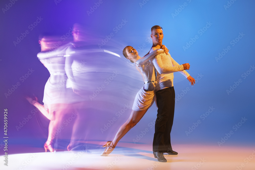 Young graceful dancers, flexible man and woman dancing ballroom dance isolated on gradient blue purple background in neon mixed light