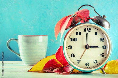 Daylight Savings Time concept, fall back in autumn. A retro alarm clock with a cup of coffee and autumn leaves on a blue backgroundn with a place for text photo