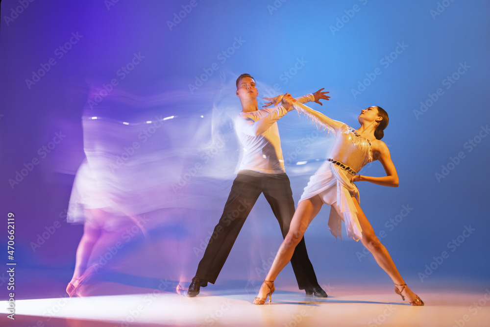 Obraz premium Two young graceful dancers, flexible man and woman dancing ballroom dance isolated on gradient blue purple background in neon mixed light