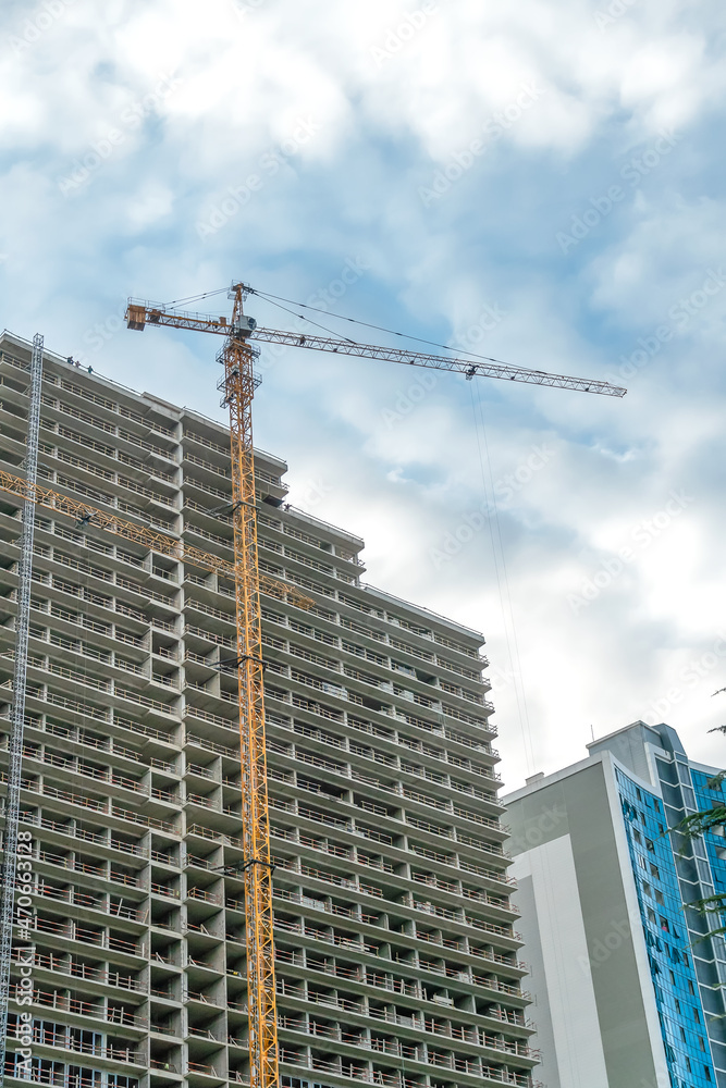Construction crane on the background of a multi-storey building under construction on a cloudy day. Vertical photo Construction crane on the background of a multi-storey building under construction on a cloudy day. Vertical photo