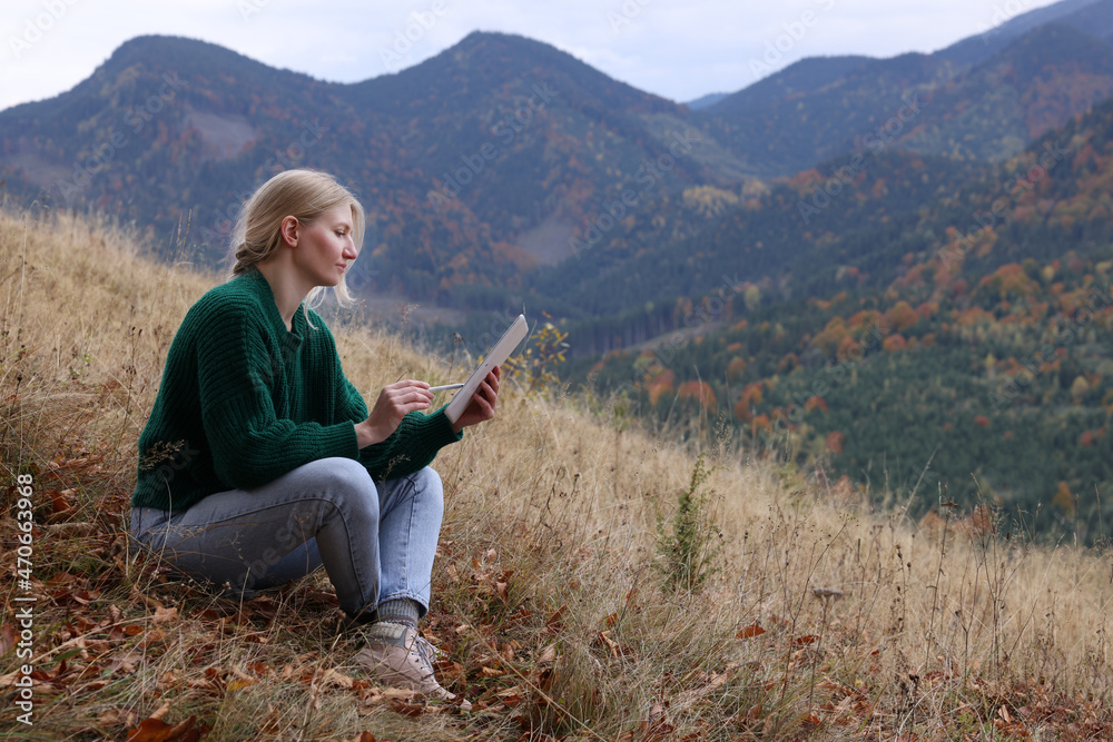 Young woman drawing on tablet in mountains, space for text Young woman drawing on tablet in mountains, space for text