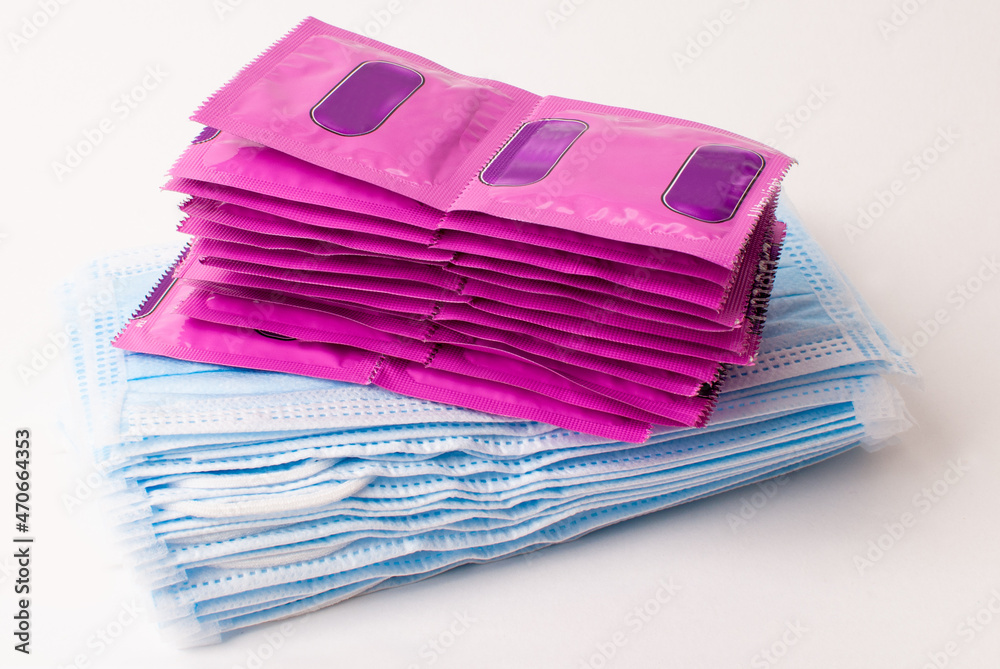 Whole packs of pink condoms and a stack of medical masks on a light background. Virus protection. Whole packs of pink condoms and a stack of medical masks on a light background. Virus protection.