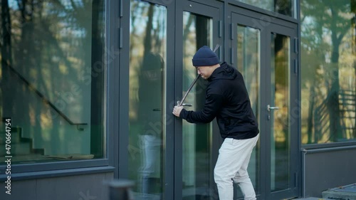 A thief burglar broke the open door of a house or office by breaking into the middle. The bandit sneaks into the building. intruder trying to force a door lock using a crowbar photo