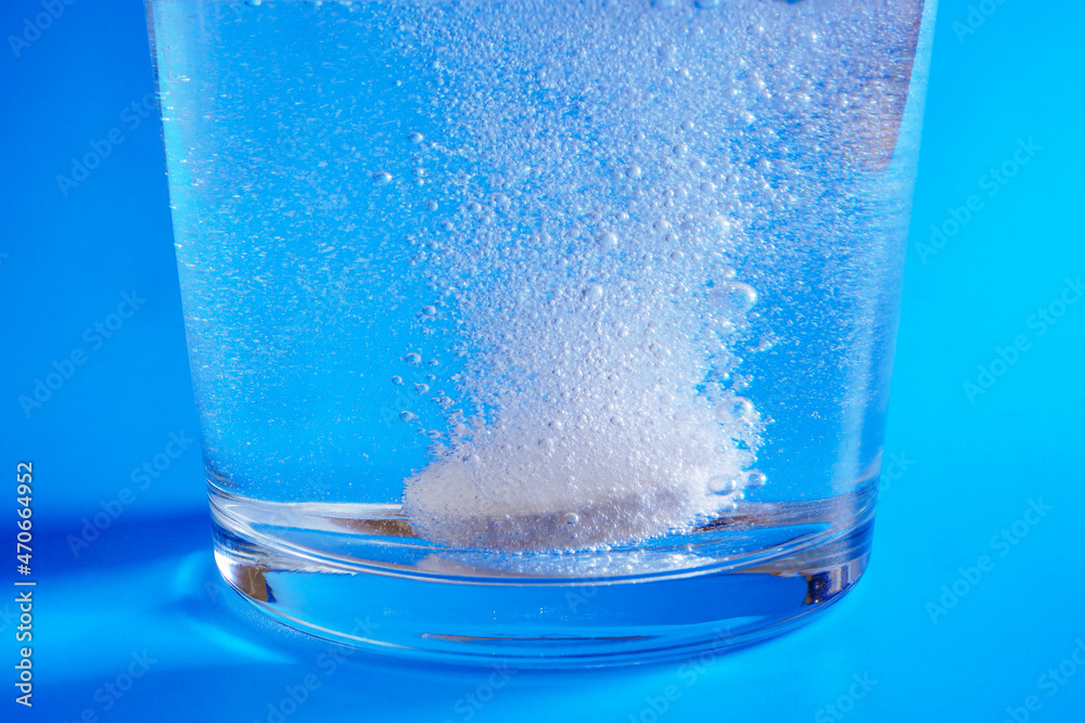 Closeup of effervescent tablet dissolving in glass of water on blue  background Photos | Adobe Stock