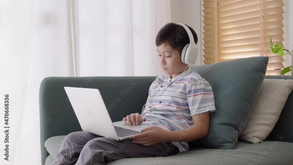 Asian little boy video call online via internet tutor on computer laptop with headphone Asian little boy video call online via internet tutor on computer laptop with headphone