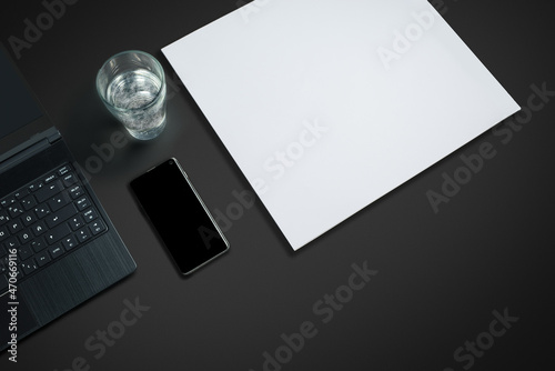 laptop on a dark desk with paper, smartphone and  a glas of sparkling water
