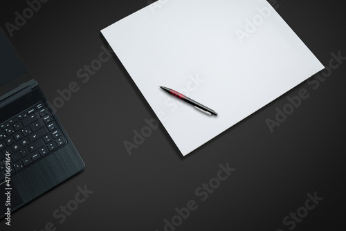 laptop on a dark desk with paper and pen