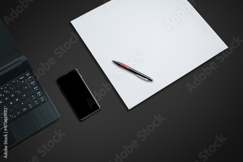 laptop on a dark desk with paper smartphone and pen