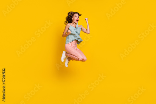 Full body photo of positive cheerful woman jump up winner good mood enjoy isolated on yellow color background