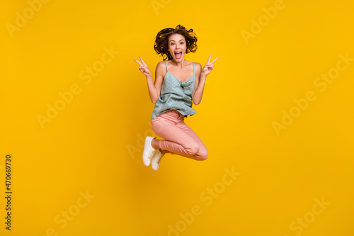 Full length photo of excited happy woman jump up show v-signs smile cool isolated on yellow color background