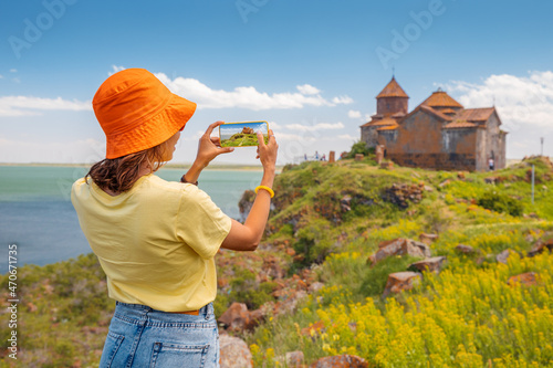 Happy woman tourist taking pictures of a famous Armenian Hayravank Monastery and Sevan Lake. Travel blogger concept photo