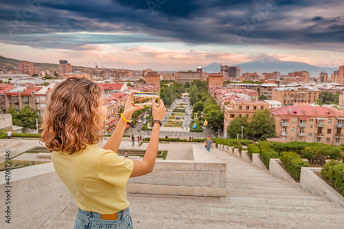 Happy woman taking pictures of a scenic urban landscape in Yerevan city with a distant view of famous Mount Ararat and Cascade complex photo