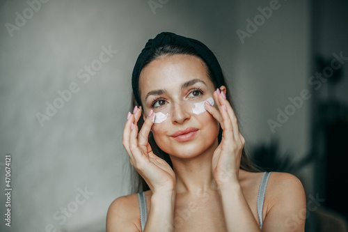 Smiling brunette 30 years old with long hair in lingerie stands at home in the bathroom and applies cream to her face