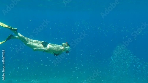 Woman in mask and fins dives underwater and looks at on large school of small fishes. Female snorkeler swim underwater in sun rays (4K-60fps) photo