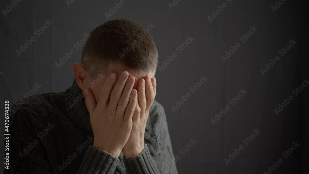 A man in a depressed state is crying while sitting on a black background covering his face with his hands. A man in a depressed state is crying while sitting on a black background covering his face with his hands.