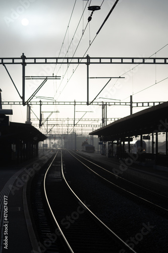 Brouillard dans la gare de Romont en Suisse, photo en contre jour avec les voies et les poteaux.