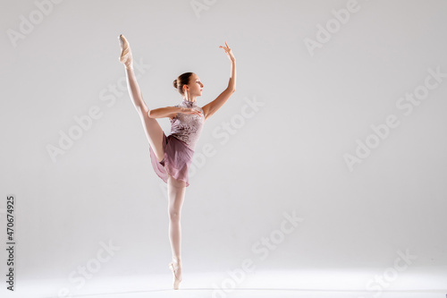 Beautiful young girl ballerina in pointe shoes and pink swimsuit on light background.
