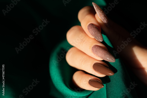 Female hand with a beautiful long nails in brown and shimmer color on a green silk background