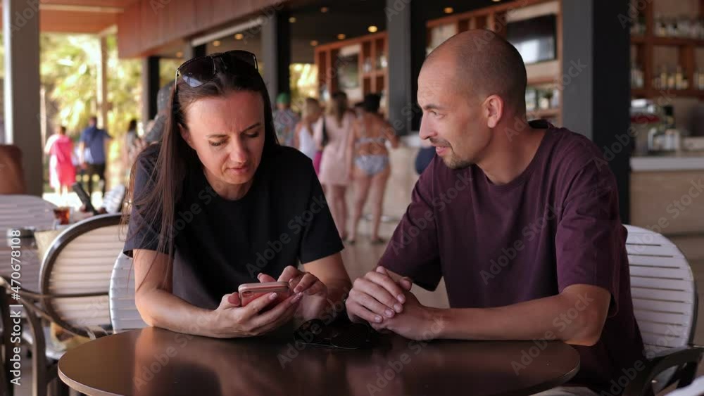 Portrait of a couple in love in a cafe in summer with a phone, in the background there are a lot of people at the hotel bar.