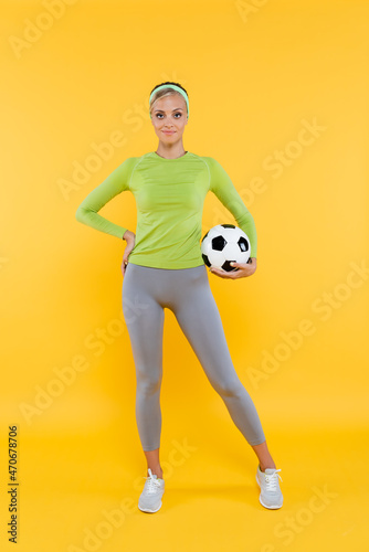 Fototapeta Naklejka Na Ścianę i Meble -  full length view of sportswoman standing with hand on hip and soccer ball on yellow