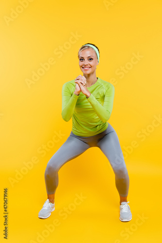 Fototapeta Naklejka Na Ścianę i Meble -  full length view of smiling woman in sportswear doing sit ups with clenched hands on yellow