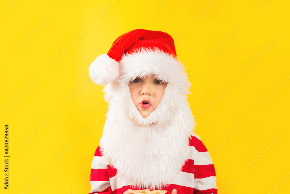 Funny child toddler in a Santa hat with red gift , yellow background. Holidays, Traditions, Christmas concept.